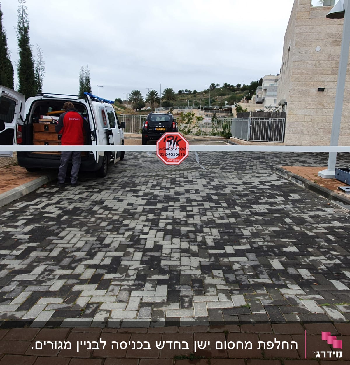 שער חשמלי עם מחסום לבן ומתקין ליד רכב מסחרי